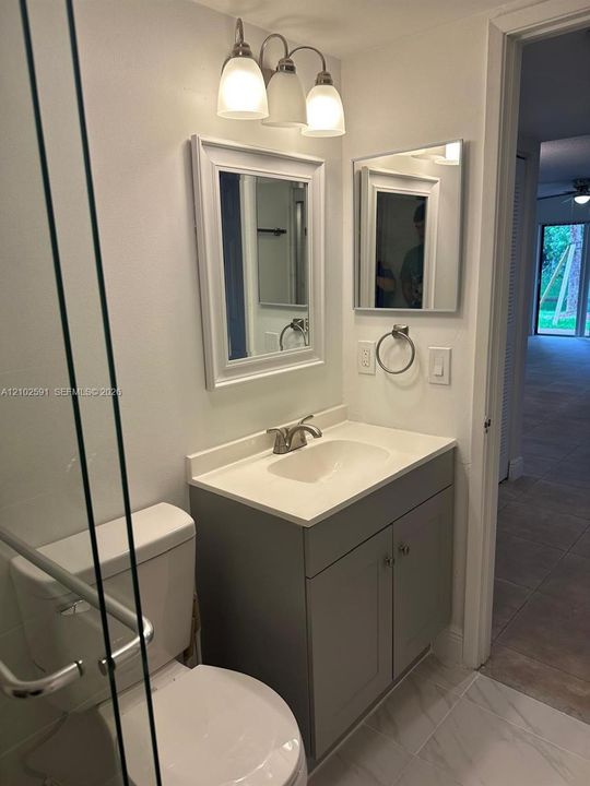 Bathroom featuring a vanity with a white countertop and integrated basin, gray shaker-style cabinetry, a framed rectangular mirror, a three-light vanity fixture, and a glass-enclosed shower