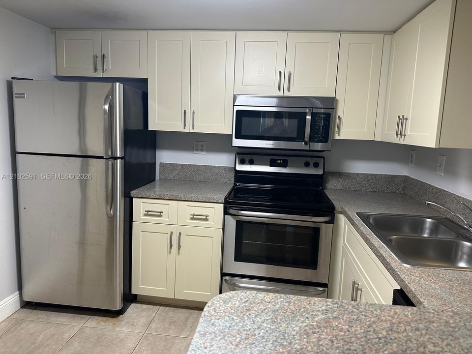 Kitchen featuring shaker-style cabinetry, stainless steel appliances, stone-finish countertops, and a double-basin stainless steel sink