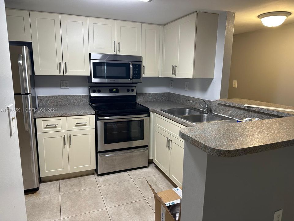 Kitchen featuring shaker-style cabinetry, stainless steel appliances, stone-finish countertops, dual-basin stainless steel sink, and ceramic tile flooring