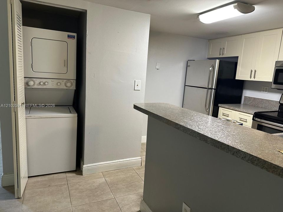 Stacked laundry unit, peninsula countertop, light-colored cabinetry, and stainless steel appliances