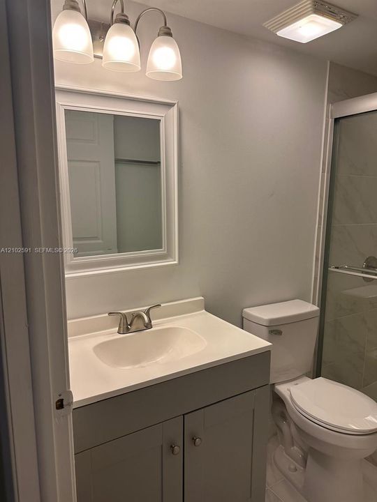Bathroom vanity with a white countertop and basin, three-light fixture, framed wall mirror, and a glass-enclosed shower