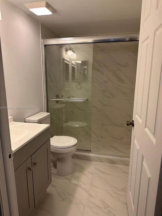 Bathroom featuring a vanity with an integrated countertop, a walk-in shower with a sliding glass door, and stone-finish wall and floor tile