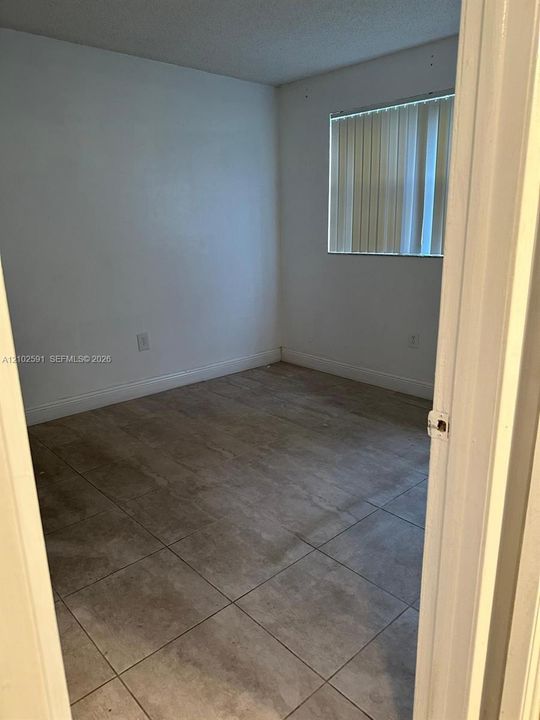 Interior room featuring large-format ceramic tile flooring, neutral wall finishes, and a window with vertical blinds