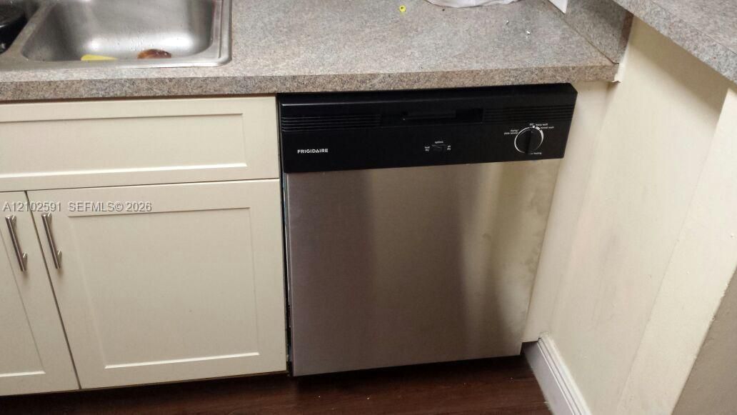 Stainless steel Frigidaire dishwasher, light-colored shaker-style cabinetry with metal pulls, and neutral solid-surface countertop with an integrated stainless steel sink