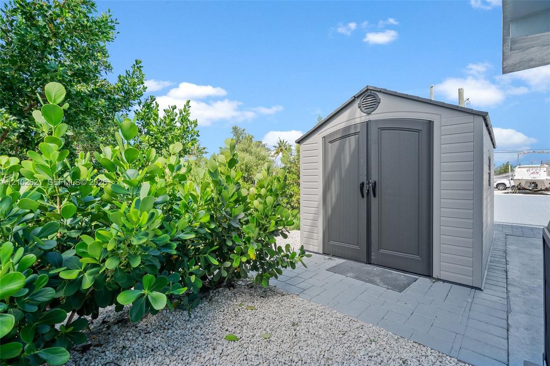 Storage shed with double doors, paved walkway, and lush perimeter landscaping