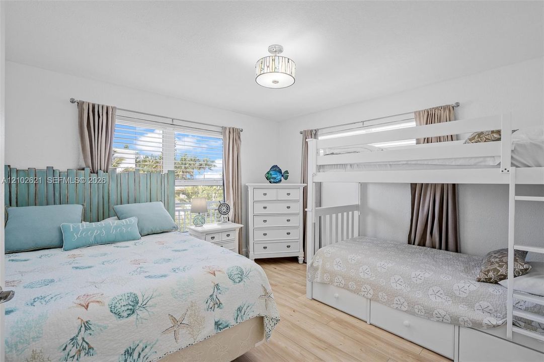 Bright room featuring wood-finish flooring, a contemporary ceiling light fixture, and windows with blinds and curtains