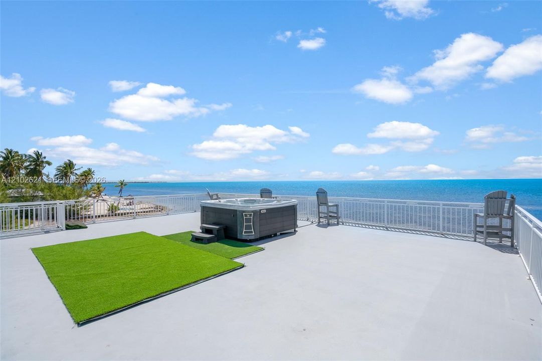 Expansive rooftop deck with a hot tub, artificial turf, and a perimeter railing