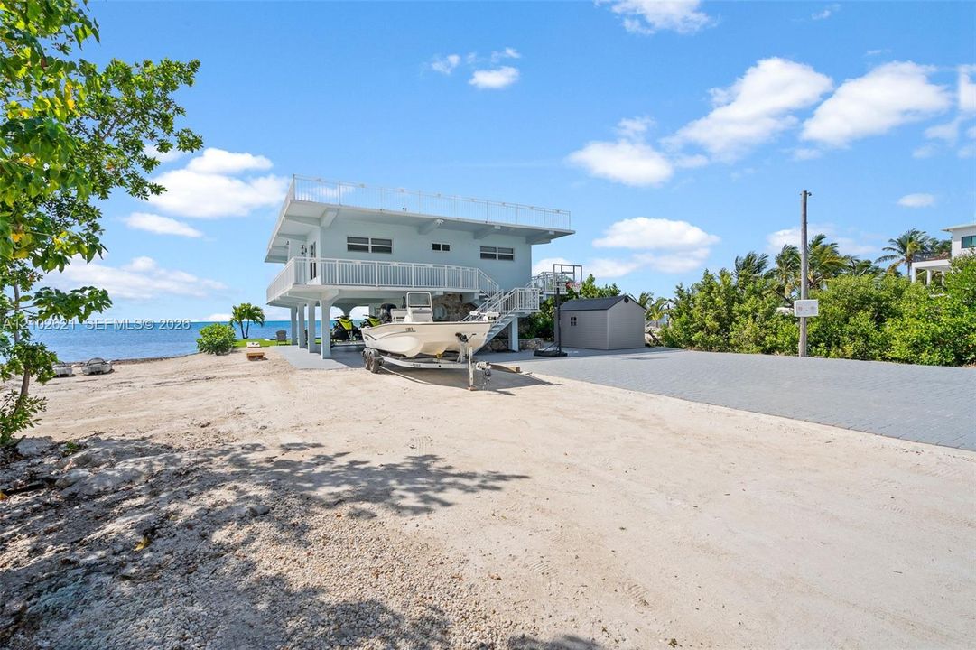 Stilted coastal residence featuring a second-story balcony with white railings, a ground-level covered area, and a gravel driveway