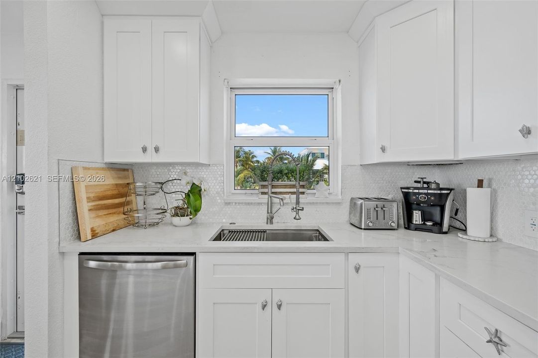 White cabinetry, stainless steel sink, white countertop, tile backsplash, and a stainless steel dishwasher