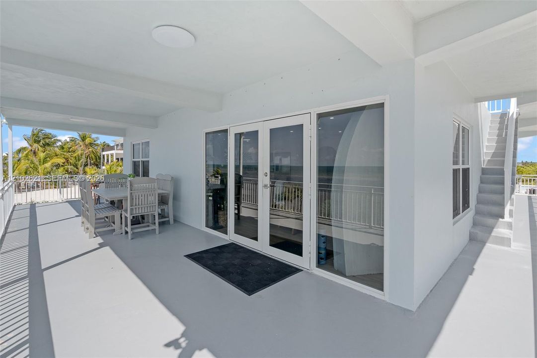 Expansive covered balcony with a white railing, large glass doors, and exterior staircase access