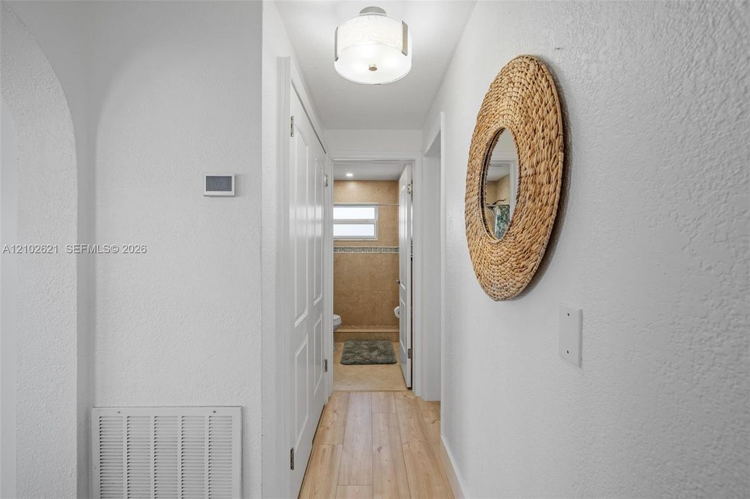 Archway entrance featuring a digital thermostat, wood-finish flooring, and overhead lighting