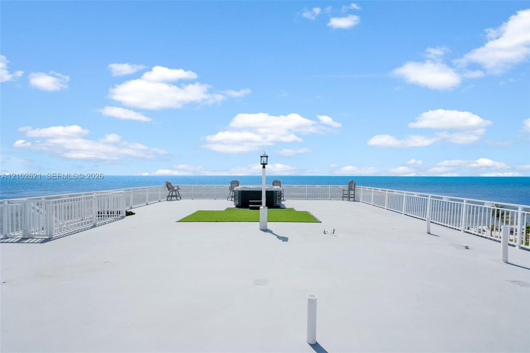 Expansive rooftop deck featuring a hot tub, artificial turf area, and perimeter white railings