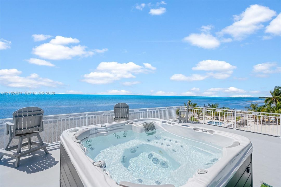 Rooftop deck featuring a hot tub, white railing, and water scenery