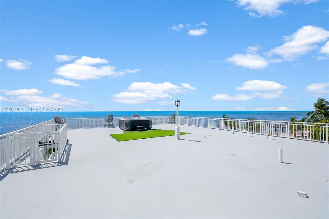 Rooftop deck featuring a hot tub, artificial turf accent, white railings, and a security gate