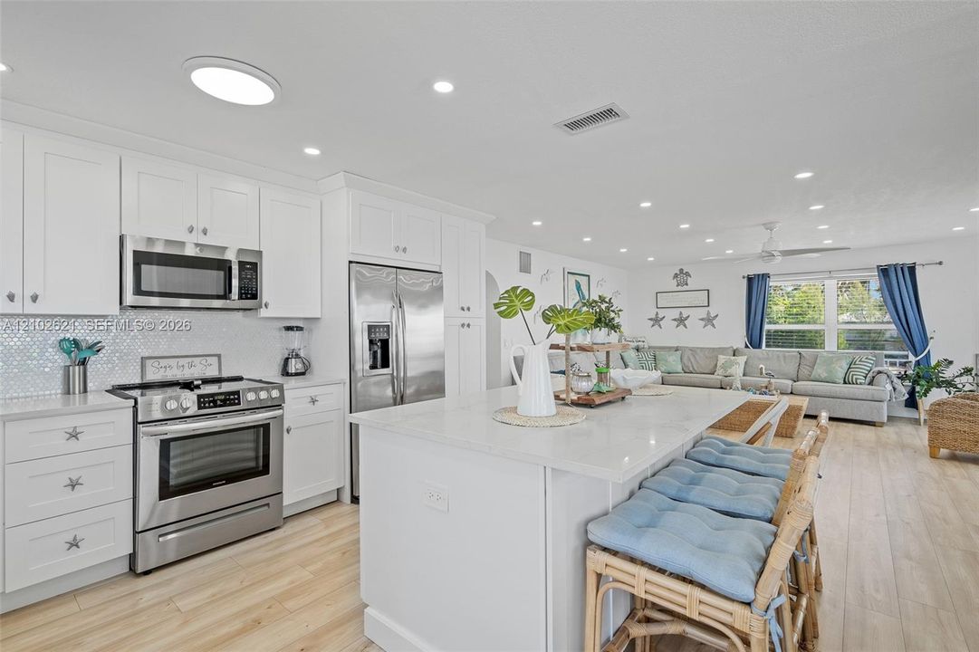Kitchen featuring white shaker cabinetry, stainless steel appliances, a white island, light-toned wood-finish flooring, and recessed lighting