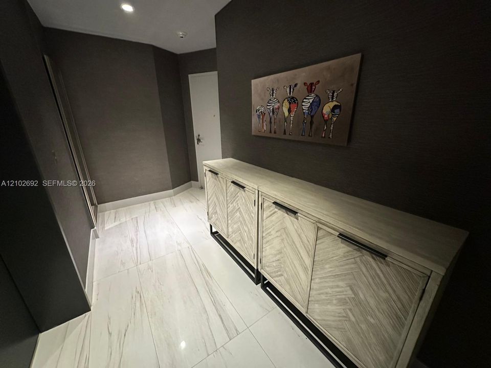Entryway featuring large-format light-toned tile flooring, deep charcoal-colored wall coverings, and recessed ceiling lighting