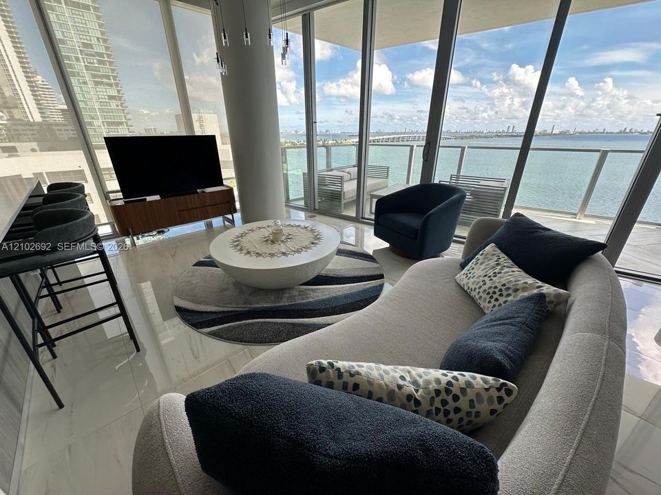 Floor-to-ceiling windows, polished light-toned flooring, cylindrical architectural column, and expansive balcony with glass railings
