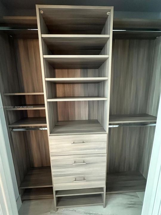 Custom storage system featuring wood-finish cabinetry, built-in shelving, three integrated drawers with metallic pulls, and stainless steel hanging rods