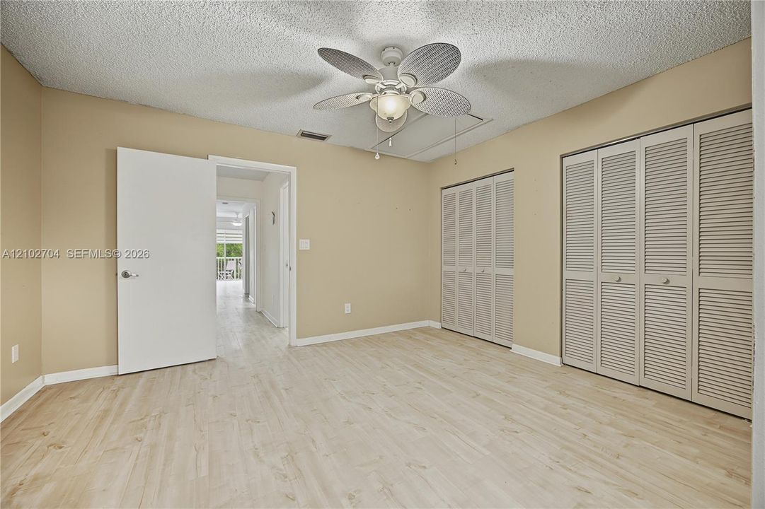 Room featuring wood-finish flooring, a ceiling fan with integrated lighting, and dual louvered-door closets
