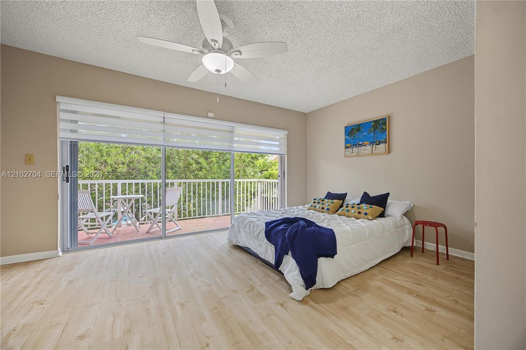 Wood-finish flooring, ceiling fan with integrated lighting, and floor-to-ceiling sliding glass doors opening to a covered balcony with a white railing