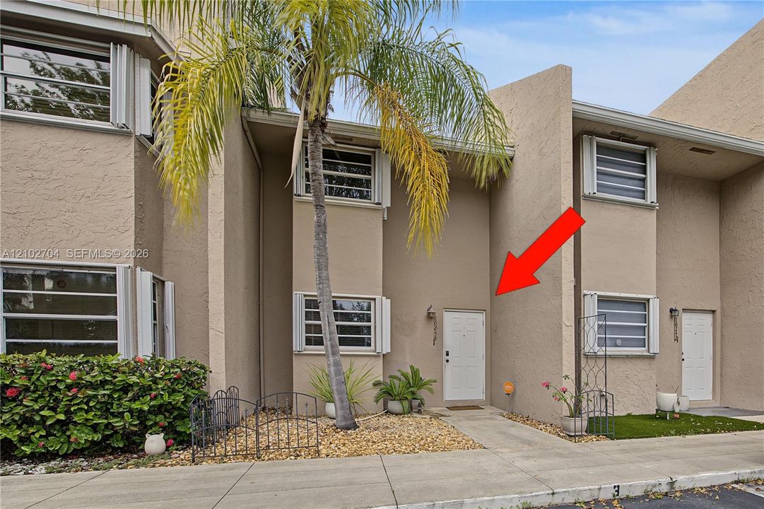 Stucco exterior featuring horizontal louvered shutters, decorative metal fencing, and a private entrance with wall-mounted lighting
