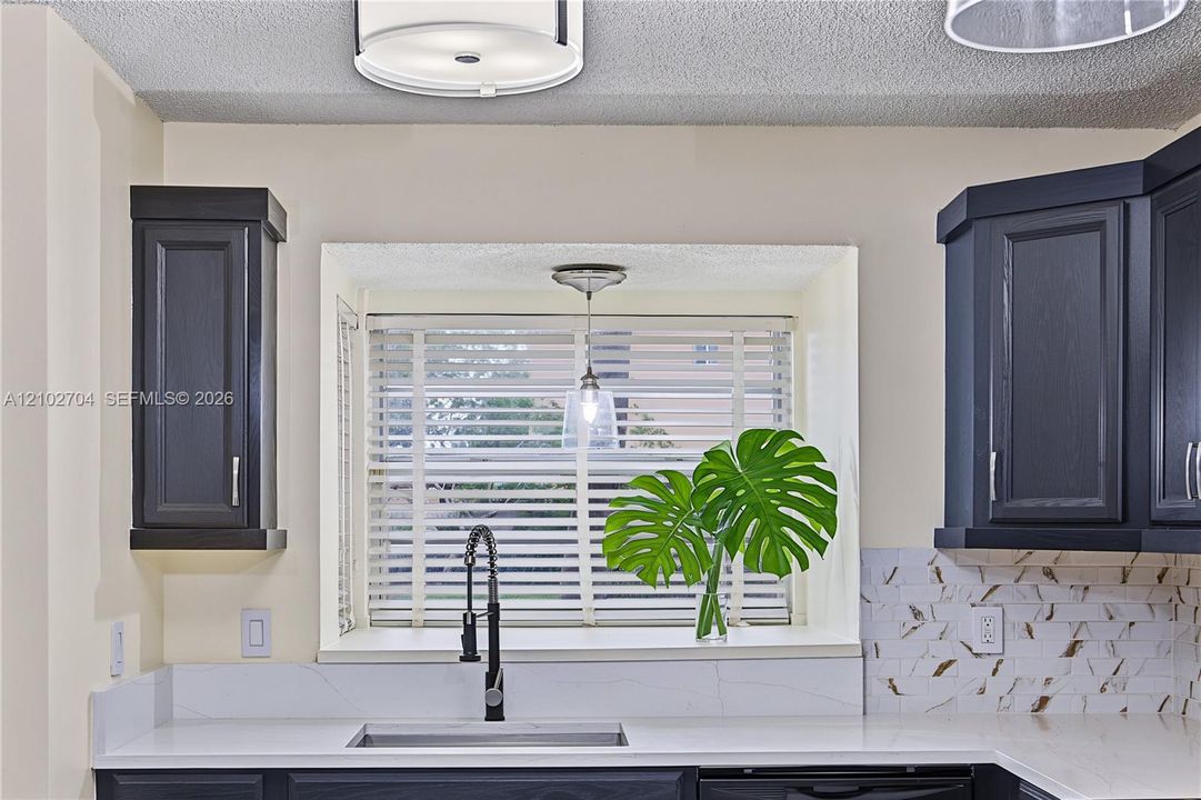 Kitchen featuring dark cabinetry, solid-surface countertops, decorative stone backsplash, undermount sink with a high-arch pull-down faucet, and a recessed window nook