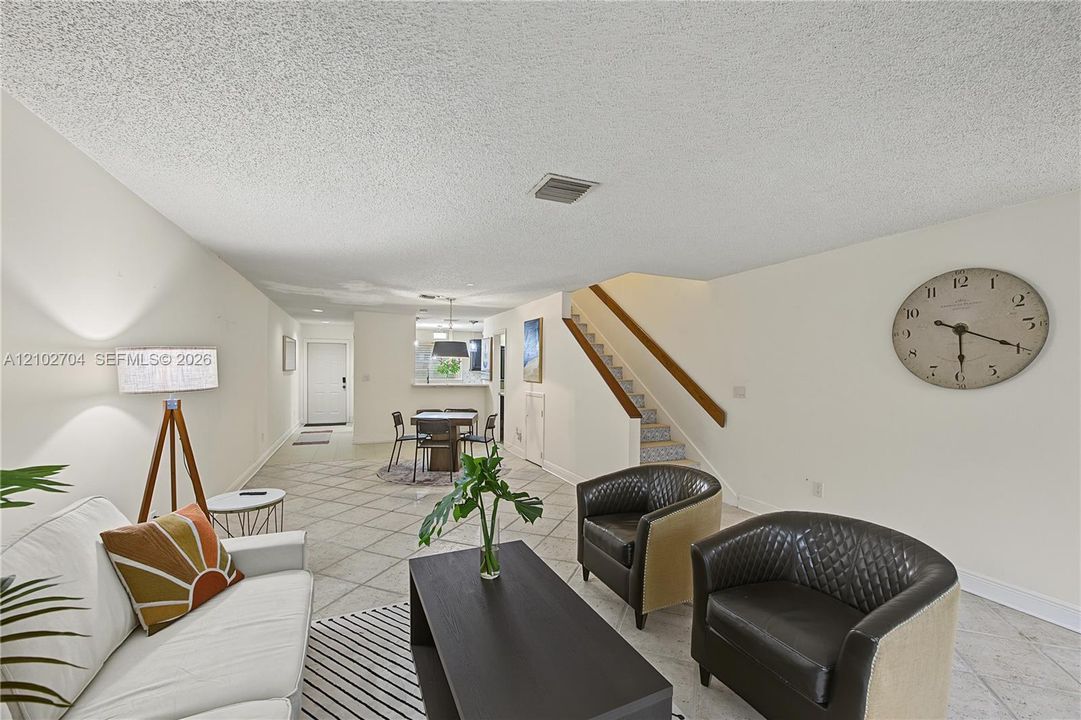 Open-concept interior featuring neutral-toned tile flooring, staircase with wood handrails, and a pass-through opening