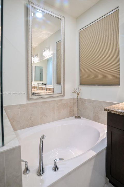Bathroom featuring tile flooring, dark-finish cabinetry with a white countertop, wall-mounted towel bar, and a tiled shower surround