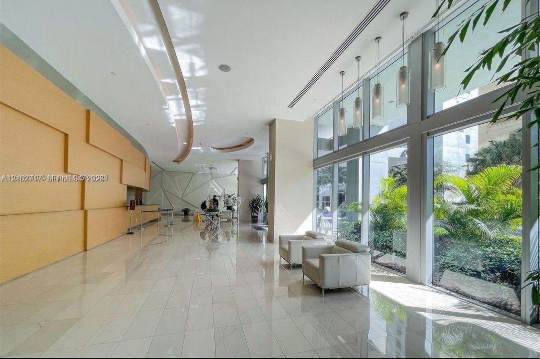 Grand lobby featuring floor-to-ceiling glass windows, polished tile flooring, wood-paneled walls, geometric architectural detailing, and tiered pendant lighting
