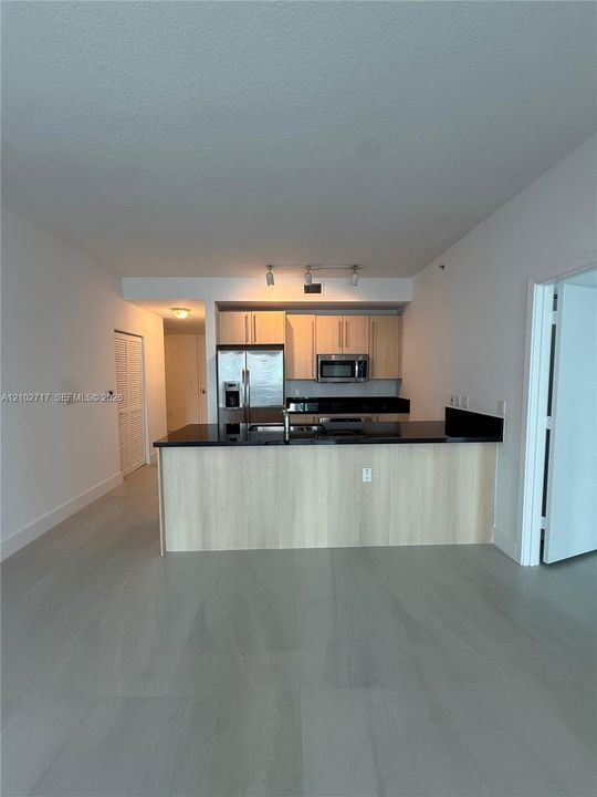 Kitchen featuring light wood-finish cabinetry, dark solid-surface countertops, a breakfast bar, stainless steel appliances, and wood-finish flooring