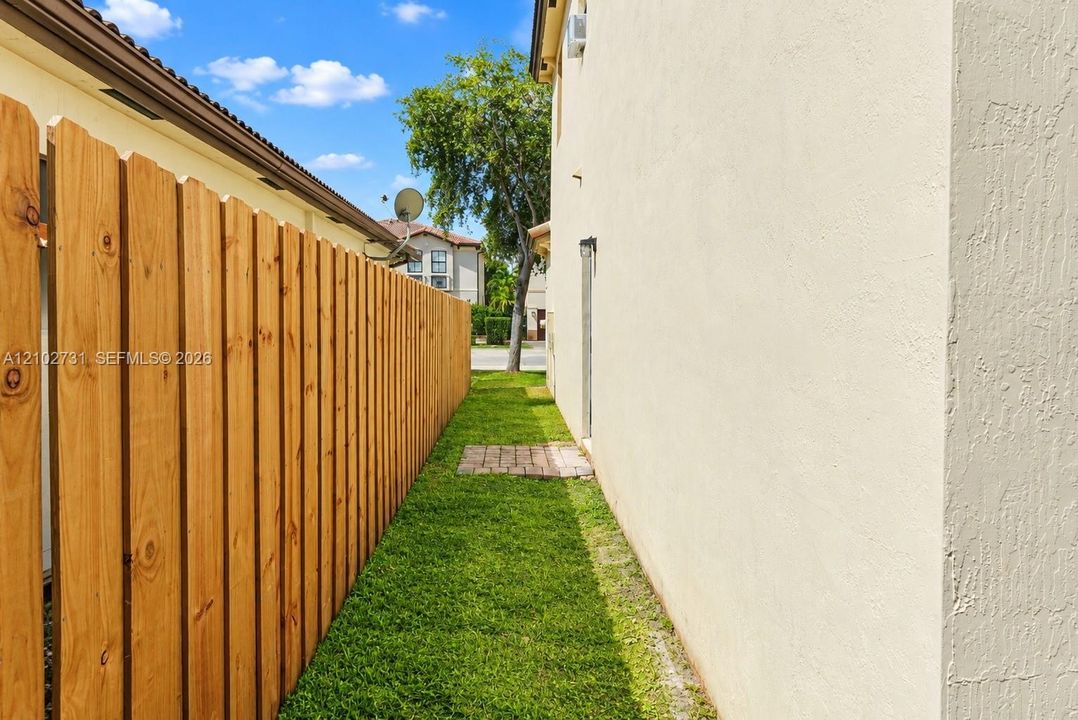 Side yard featuring a natural wood privacy fence, stucco exterior finish, and a brick paver pathway