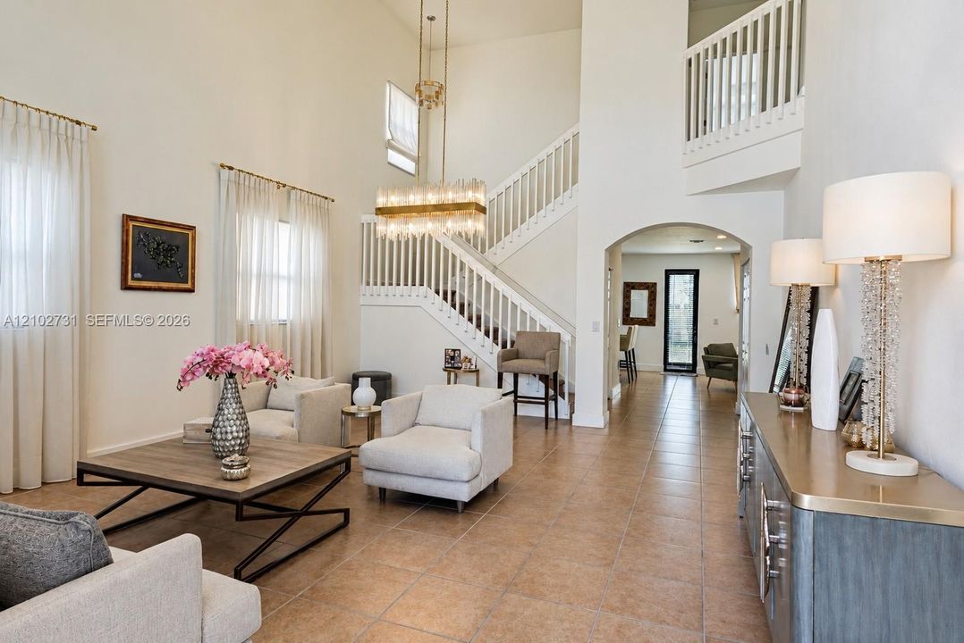 Double-height foyer featuring ceramic tile flooring, a statement crystal chandelier, a grand staircase with decorative balusters, and a prominent arched entryway