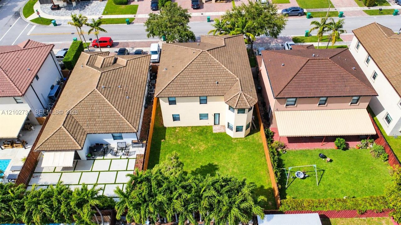 Two-story exterior featuring a hip roof, stucco facade, turret-style architectural detailing, and a fenced backyard with a lawn