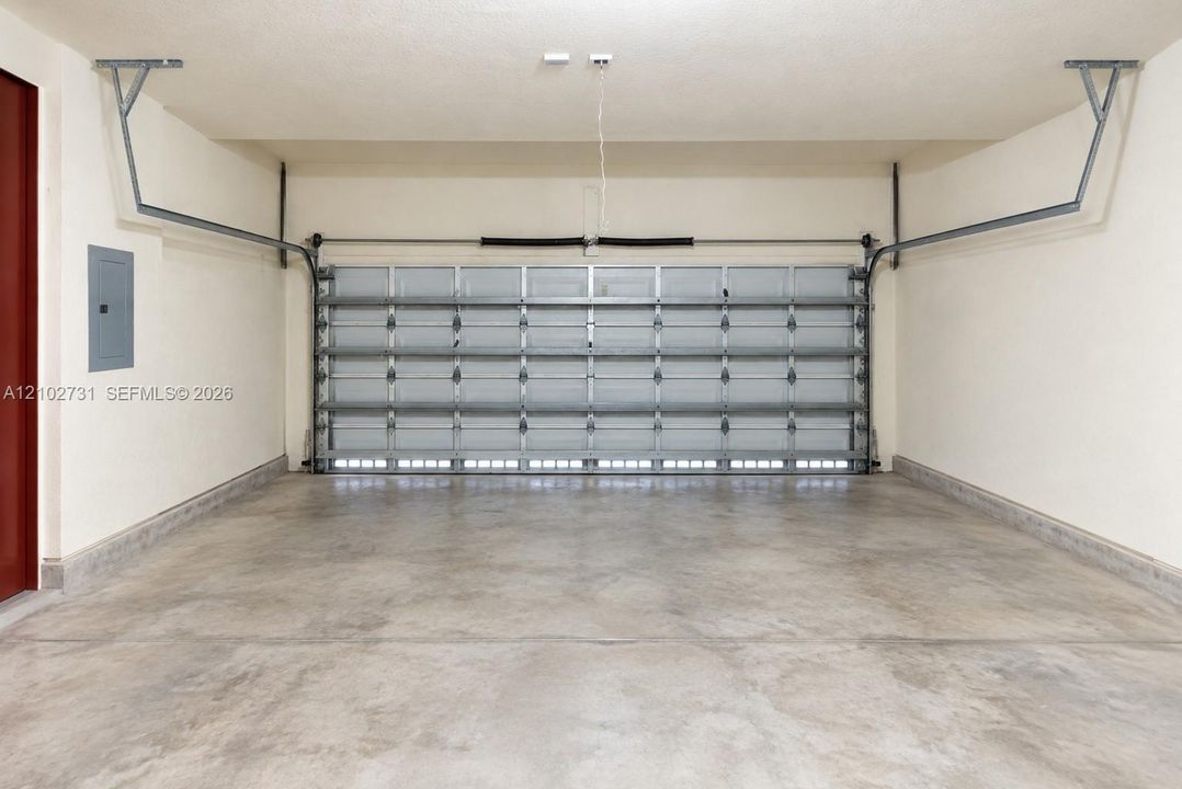 Enclosed garage featuring a multi-panel steel door, reinforced ceiling-mounted hardware, smooth-finish concrete flooring, and an integrated electrical service panel