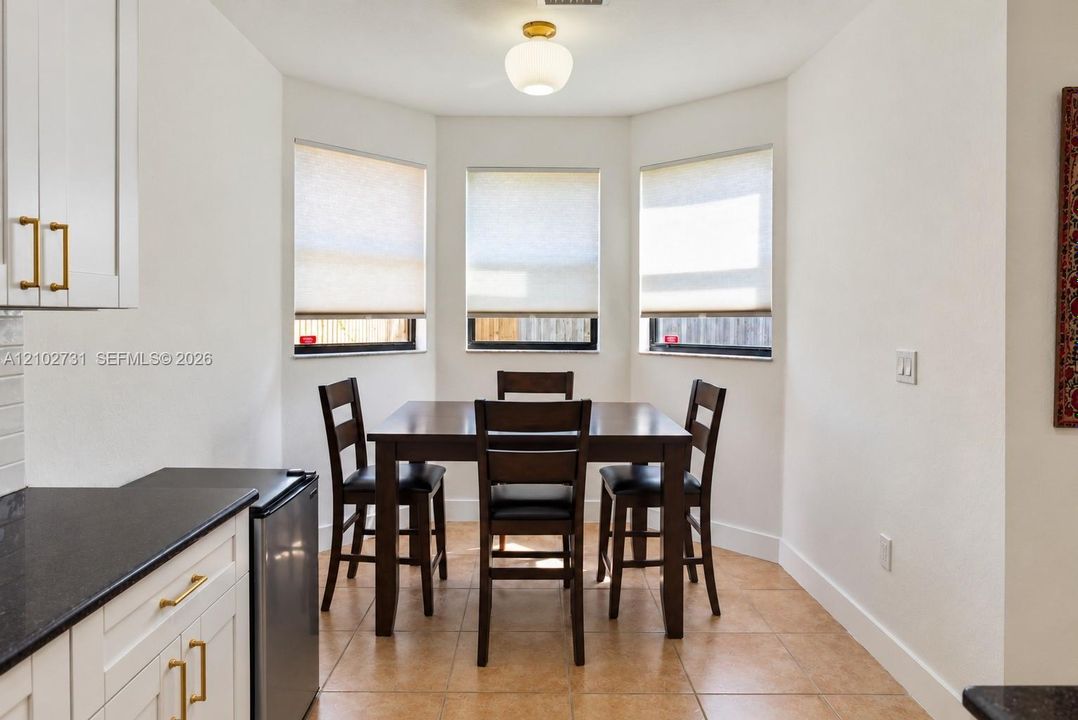 Bay window area featuring tile flooring, white shaker-style cabinetry with brass-finish hardware, dark stone-finish countertops, and a modern globe flush-mount light fixture