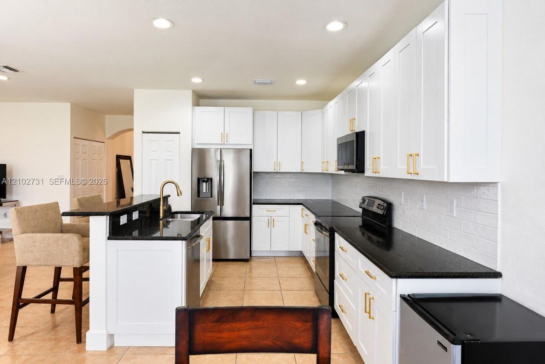 Kitchen featuring white cabinetry with gold-tone hardware, dark solid-surface countertops, subway tile backsplash, stainless steel appliances, and recessed lighting