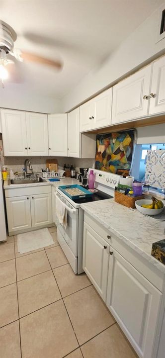 Kitchen featuring white shaker-style cabinetry, stone-patterned countertops, stainless steel sink with a high-arch faucet, integrated ceiling fan, and tile flooring