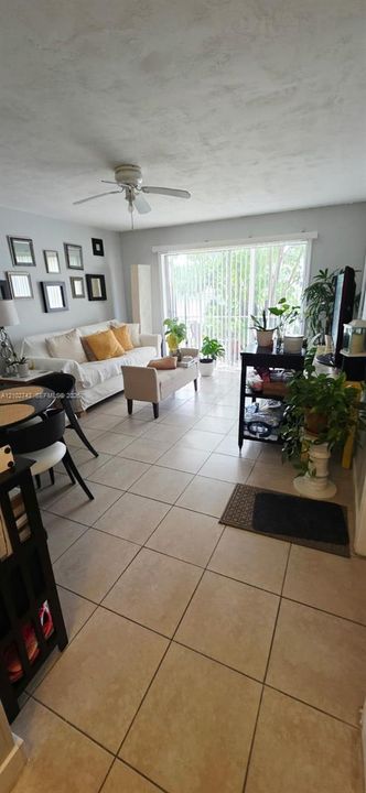 Neutral tile flooring, ceiling fan, and sliding glass door with vertical blinds