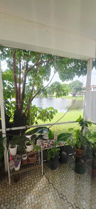 Screened lanai featuring tiled flooring, structural support pillars, and direct exterior access to a pond