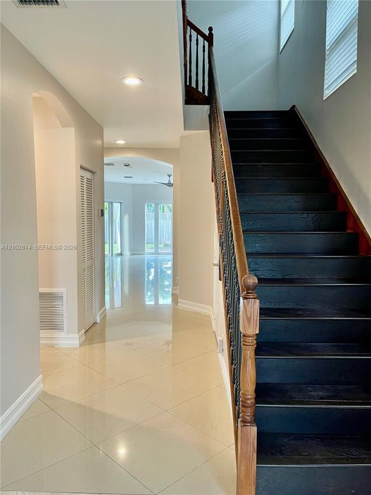 Foyer featuring large-format tile flooring, arched wall openings, and a staircase with dark wood treads and an ornate metal balustrade