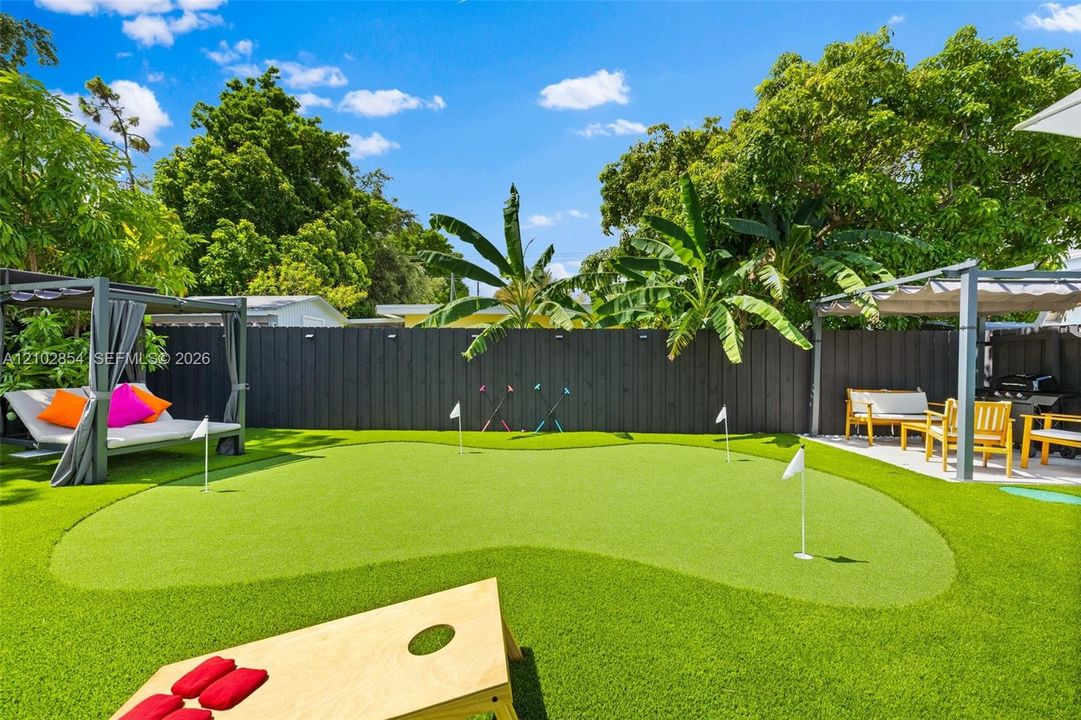 Private backyard featuring a synthetic grass putting green, dual pergola structures, and dark wood-finish privacy fencing