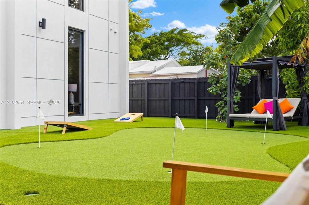 Backyard featuring synthetic turf putting green with multiple holes, modern panel-clad exterior, and perimeter privacy fencing