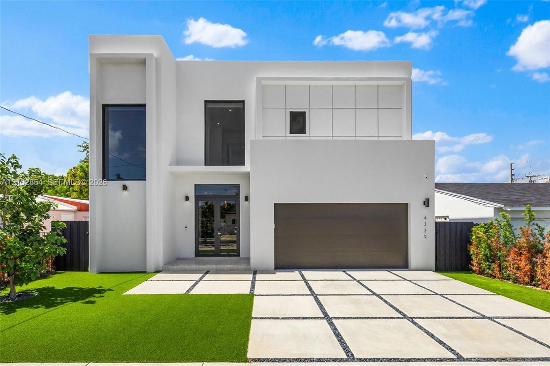 Contemporary architectural exterior featuring a smooth white stucco facade, geometric grid-patterned concrete driveway, inset glass-panel front entry door, large-format vertical windows, and square-tiled upper-level cladding