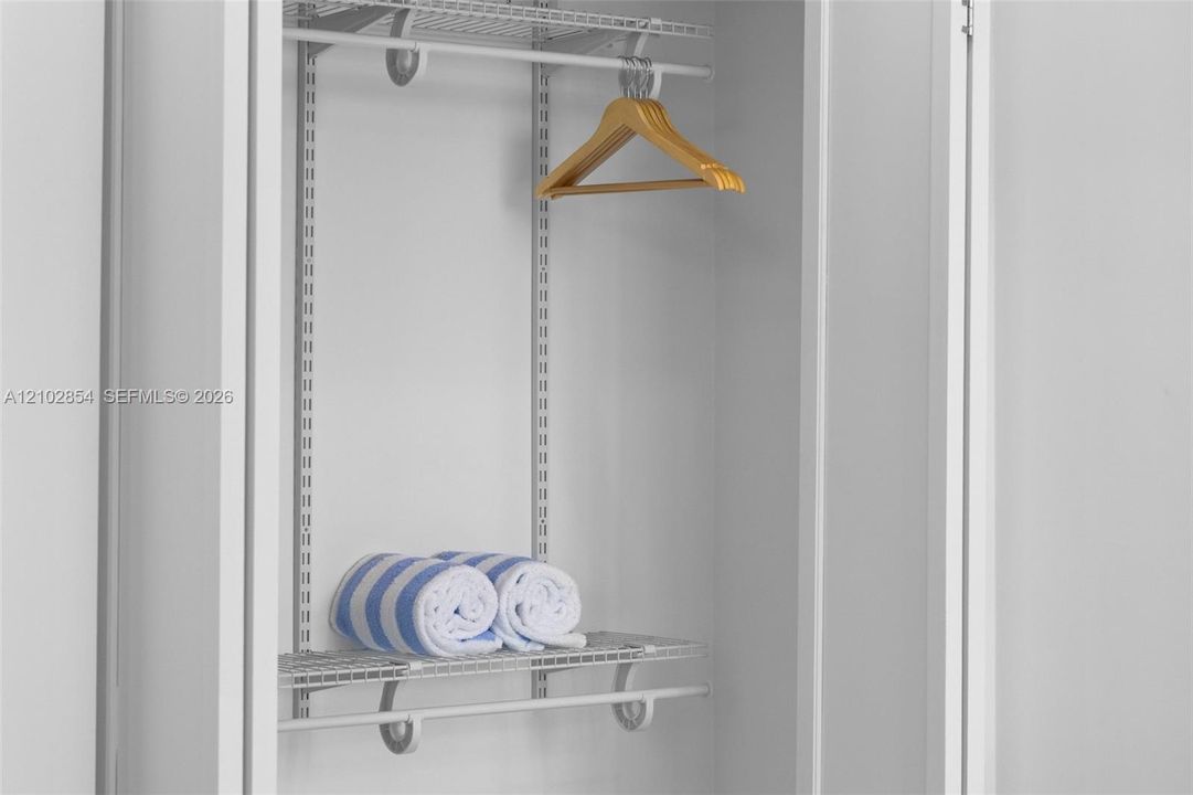 Storage closet featuring white wire shelving, adjustable wall-mounted standards, and integrated hanging rods
