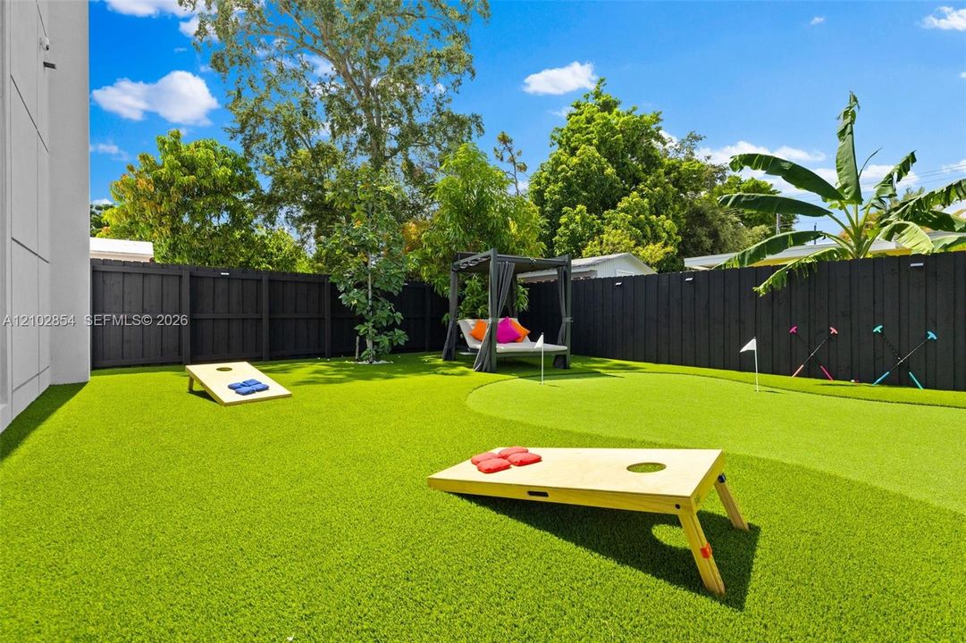Private backyard featuring artificial turf, a putting green, and a dark-stained wood privacy fence