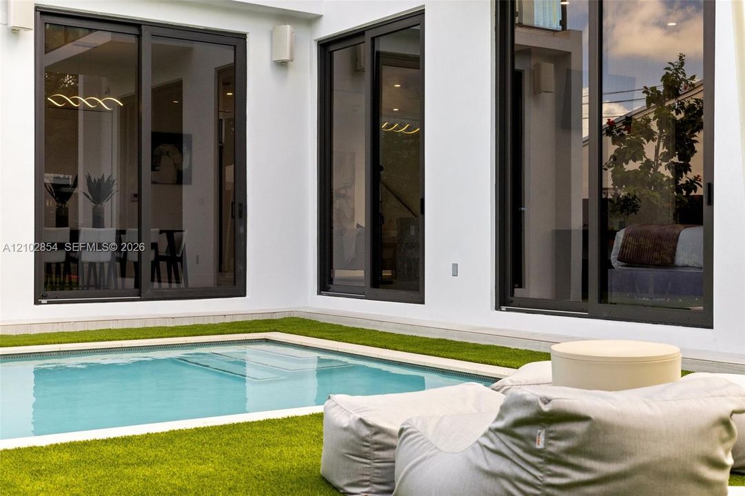 Private courtyard featuring an in-ground swimming pool, synthetic turf surround, and floor-to-ceiling sliding glass doors with dark metal frames