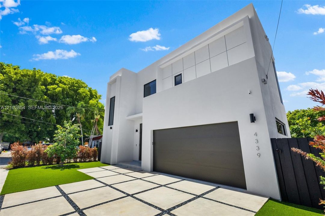 Modern minimalist exterior featuring a smooth stucco façade, segmented grid concrete driveway, attached multi-car garage, and geometric architectural detailing