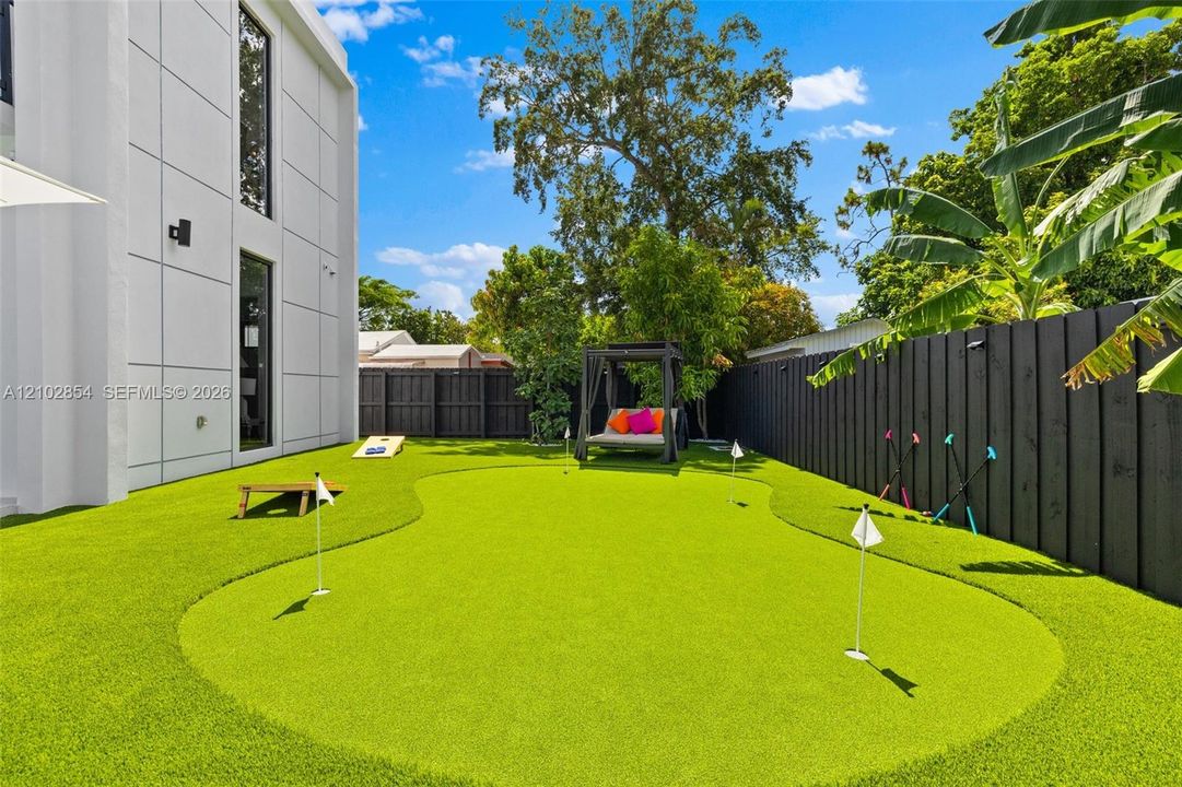 Private backyard featuring a synthetic grass putting green, solid-panel privacy fencing, and modern exterior wall cladding
