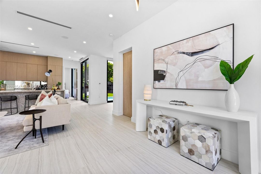 Open-concept interior featuring light-toned stone-finish flooring, recessed lighting, floor-to-ceiling cabinetry, and glass sliding doors