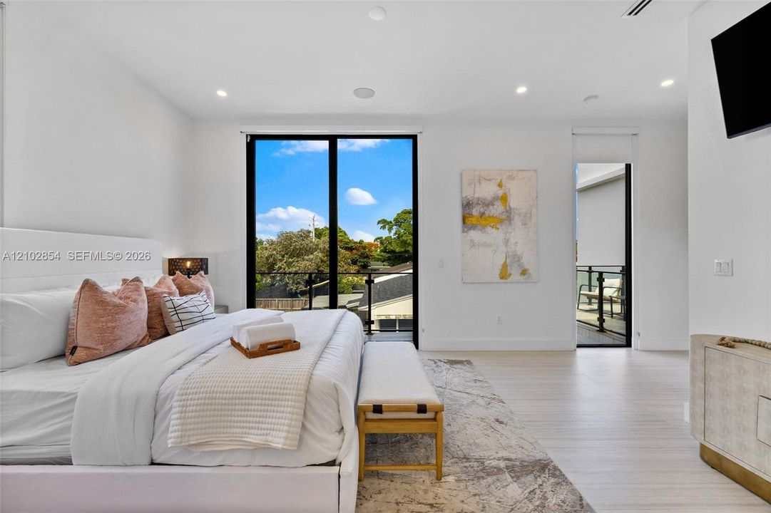 Bright interior featuring light wood-finish flooring, recessed lighting, floor-to-ceiling glass panel doors, and a private balcony with black metal railing